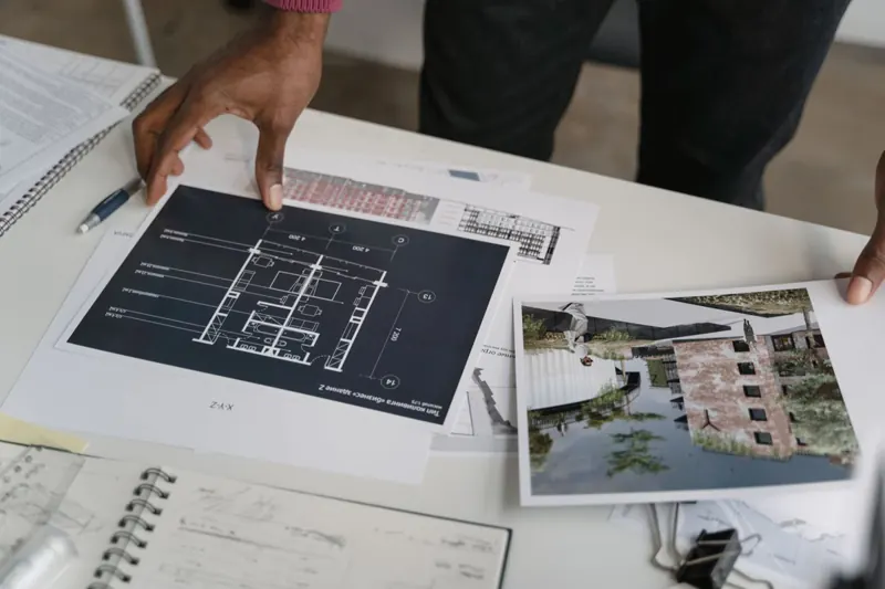 Plans et photos d'un dossier posés sur une table, une main les parcourt